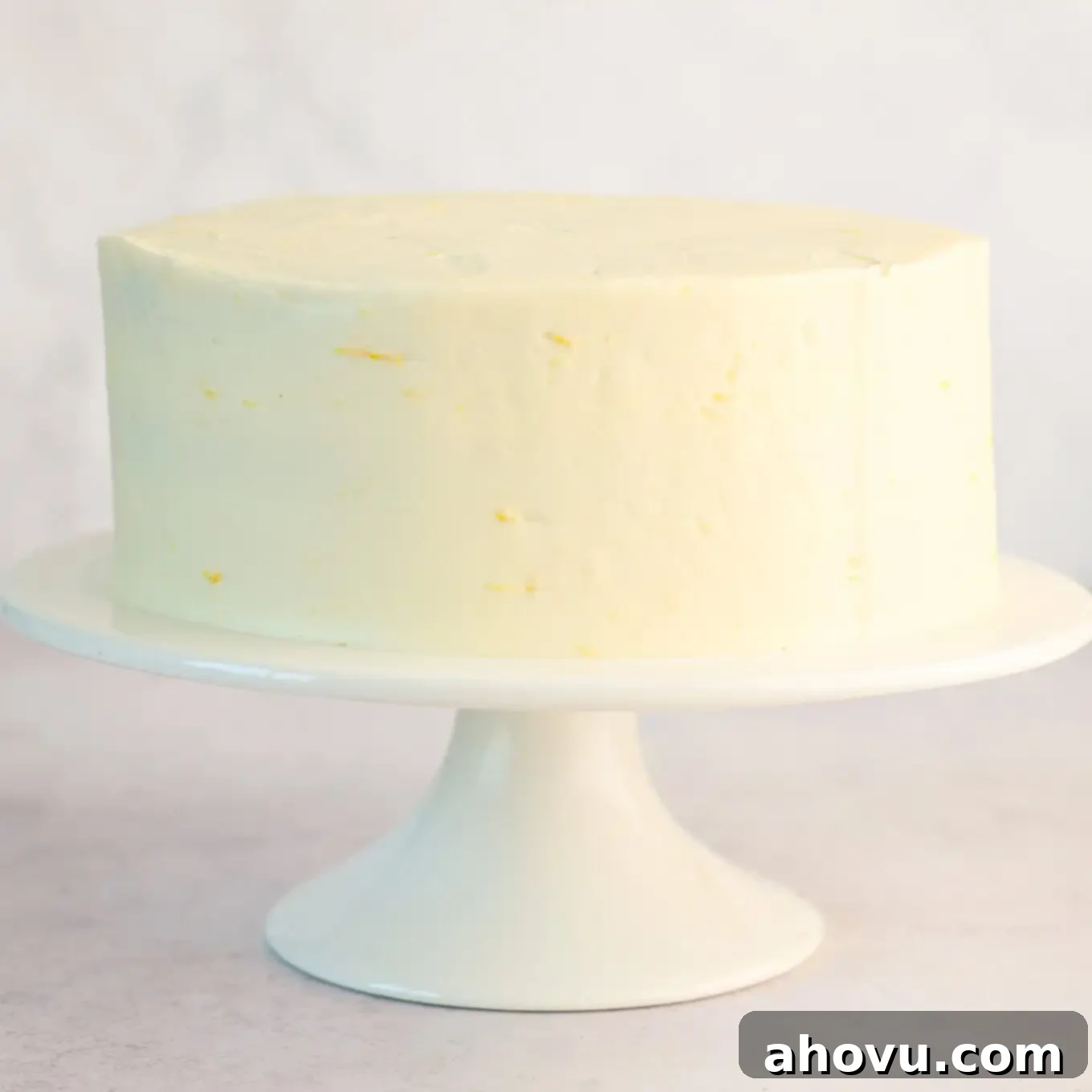 A perfectly smooth and plain frosted lemon blueberry cake on a cake stand, awaiting its final garnishes.