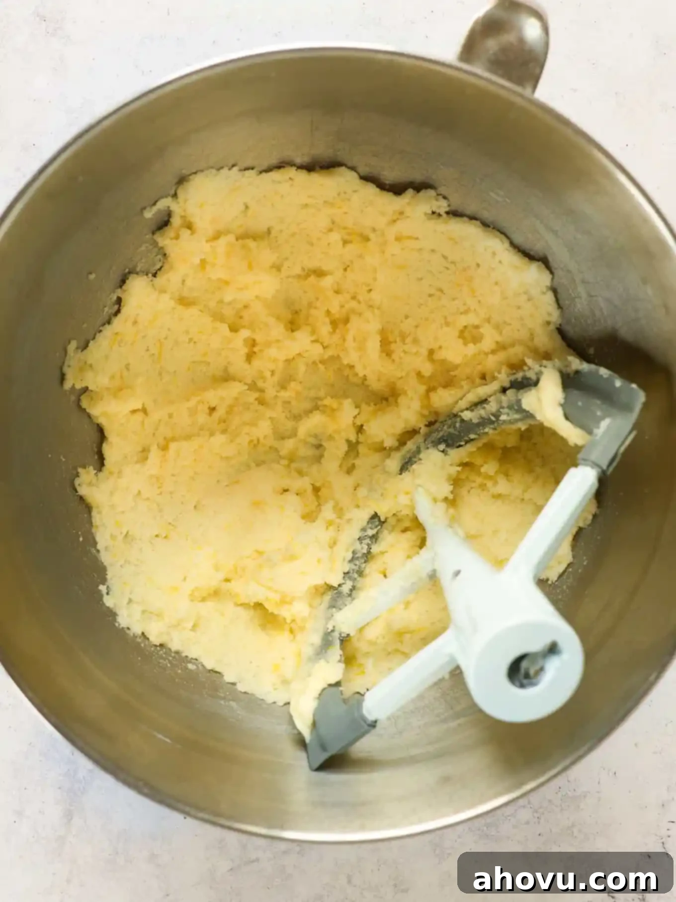 An overhead view of softened butter and granulated sugar being creamed together in a stand mixer bowl with a paddle attachment, showing a light and fluffy texture.