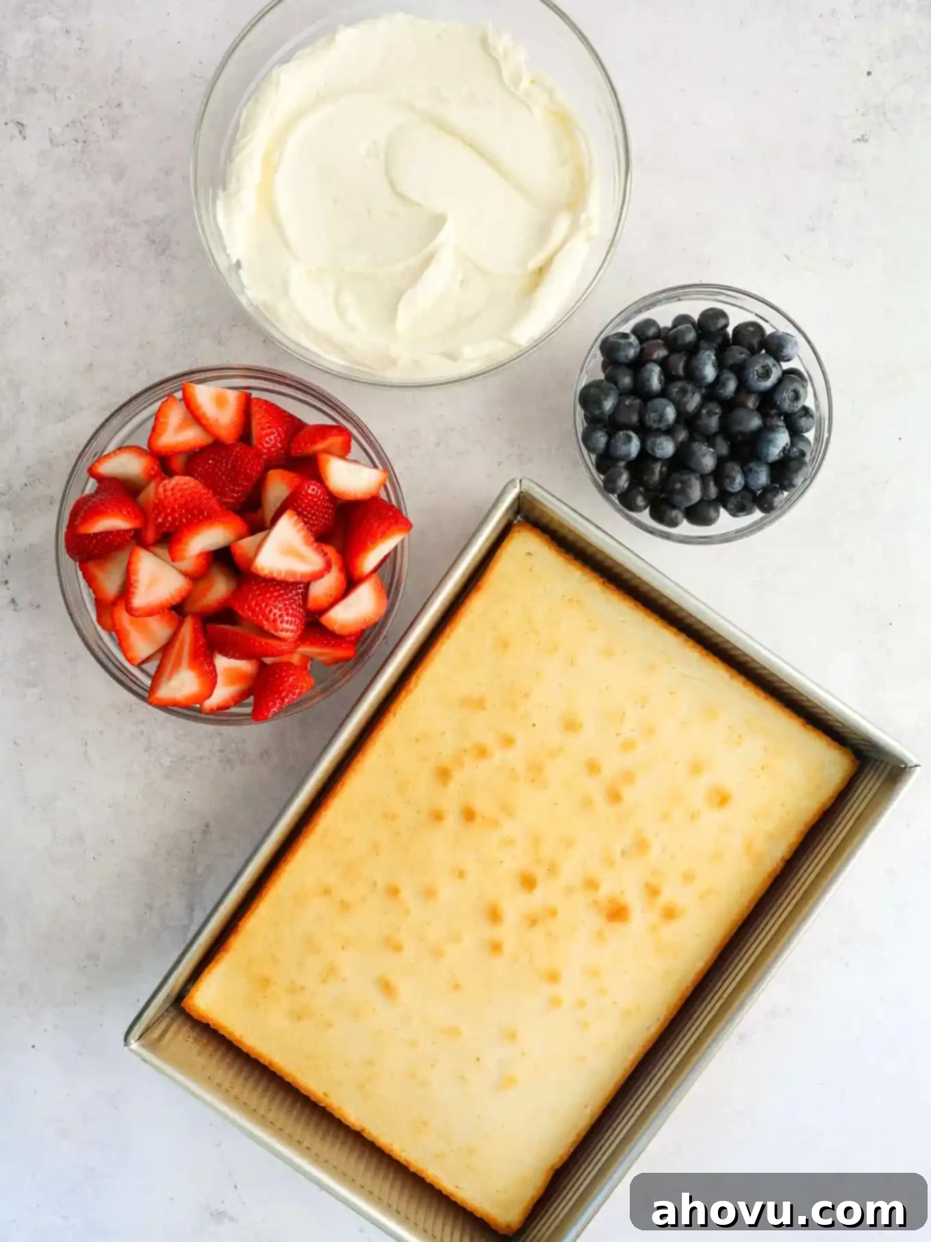 A selection of ingredients for the flag cake: a plain white cake, fresh berries, and a bowl of whipped cream cheese frosting.