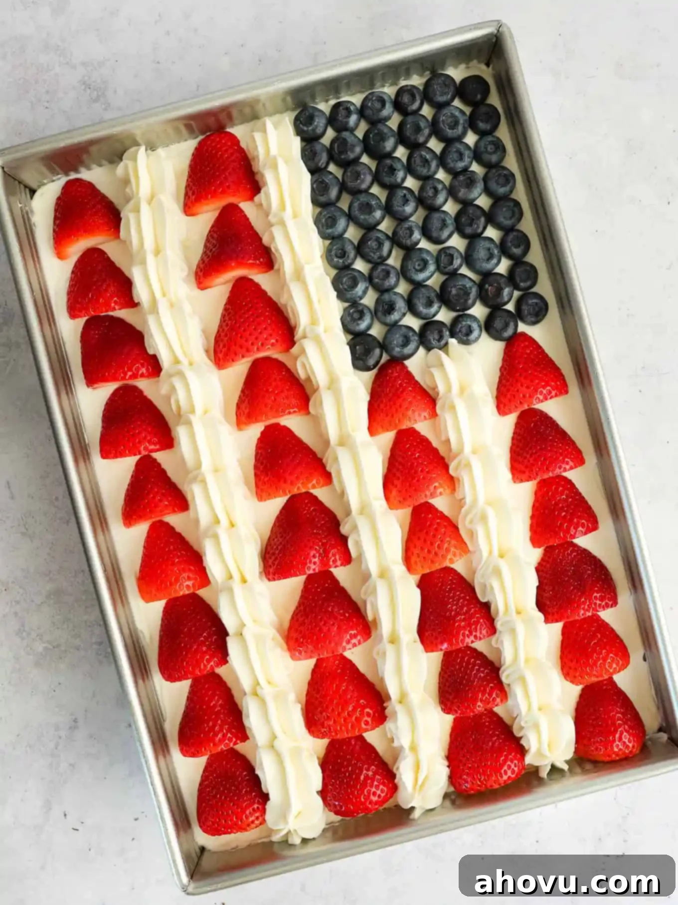 A flag cake decorated with alternating red strawberry stripes and white frosting stripes, alongside the blueberry field.