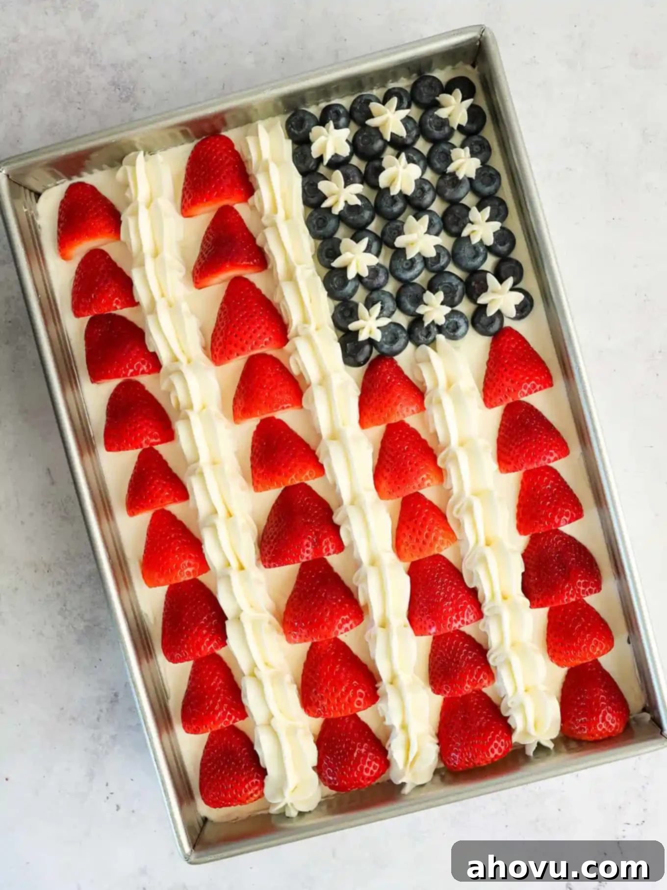 An American flag cake adorned with strawberries, blueberries, and small piped frosting stars within the blue field.