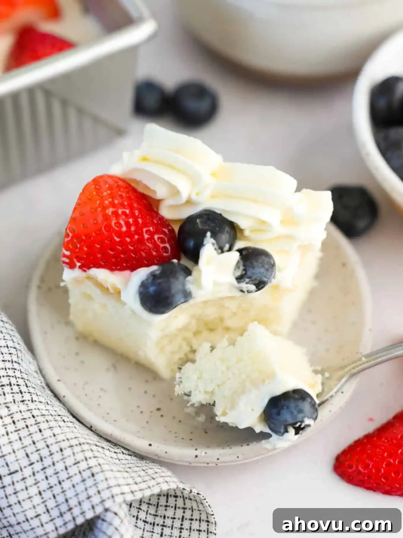 A close-up slice of white cake topped with fresh berries and cream cheese frosting, showing the layers.