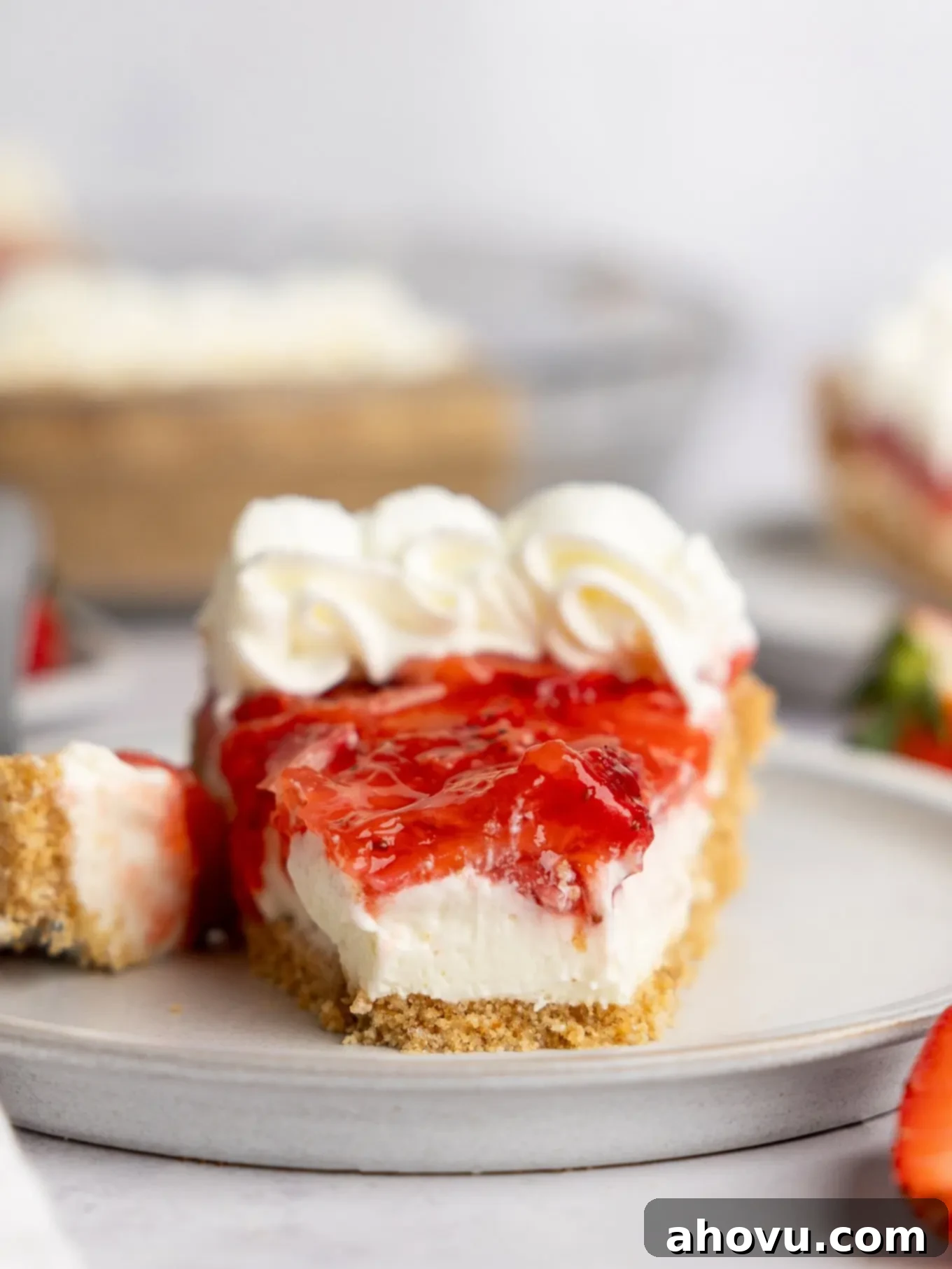 A close-up of a single slice of strawberry cream cheese pie, with a bite taken, highlighting the fluffy filling, graham cracker crust, and fresh strawberry topping.