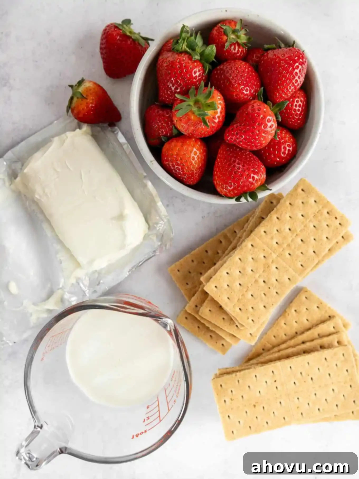 A flat lay photograph displaying all the fresh ingredients required to bake a delicious strawberry cream cheese pie, neatly arranged on a kitchen counter.