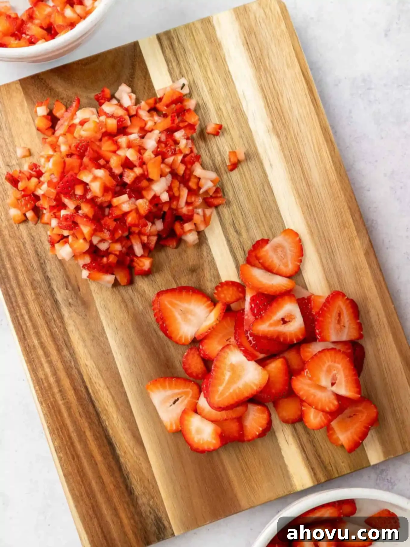 Fresh strawberries, some chopped and some sliced, arranged on a wooden cutting board, ready for the pie topping preparation.