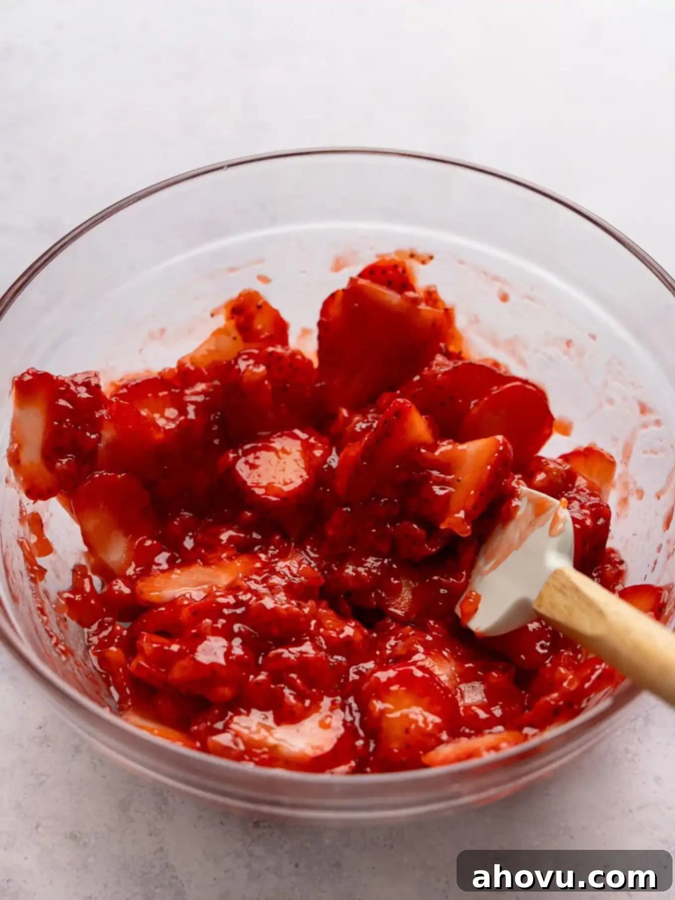 A vibrant, thick homemade strawberry topping, with both mashed and sliced strawberries, in a mixing bowl, ready to be spread over the pie.