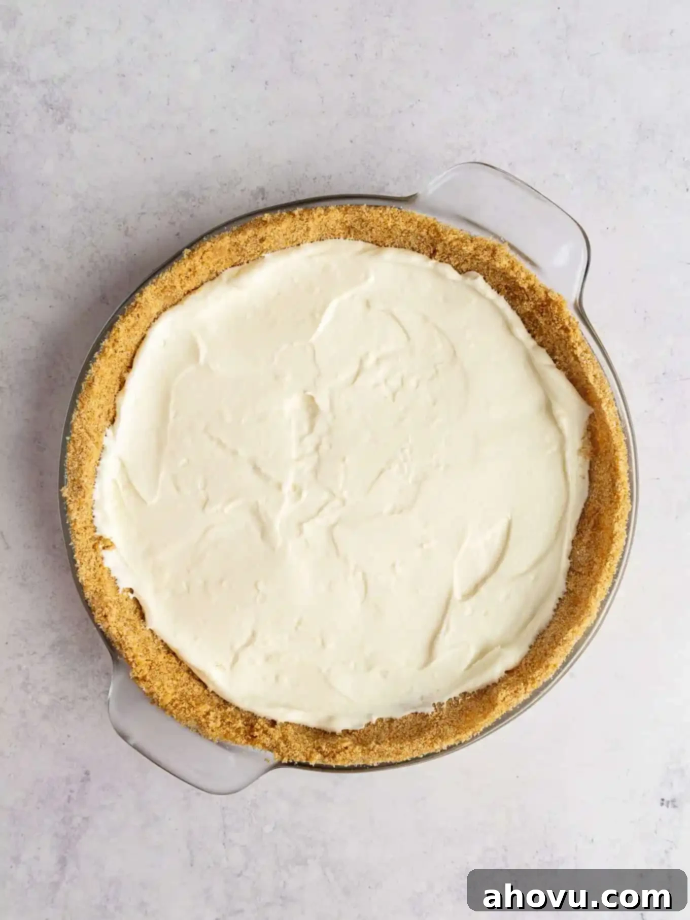 An overhead view of the luscious cream cheese filling spread evenly into the golden graham cracker crust within a pie plate.