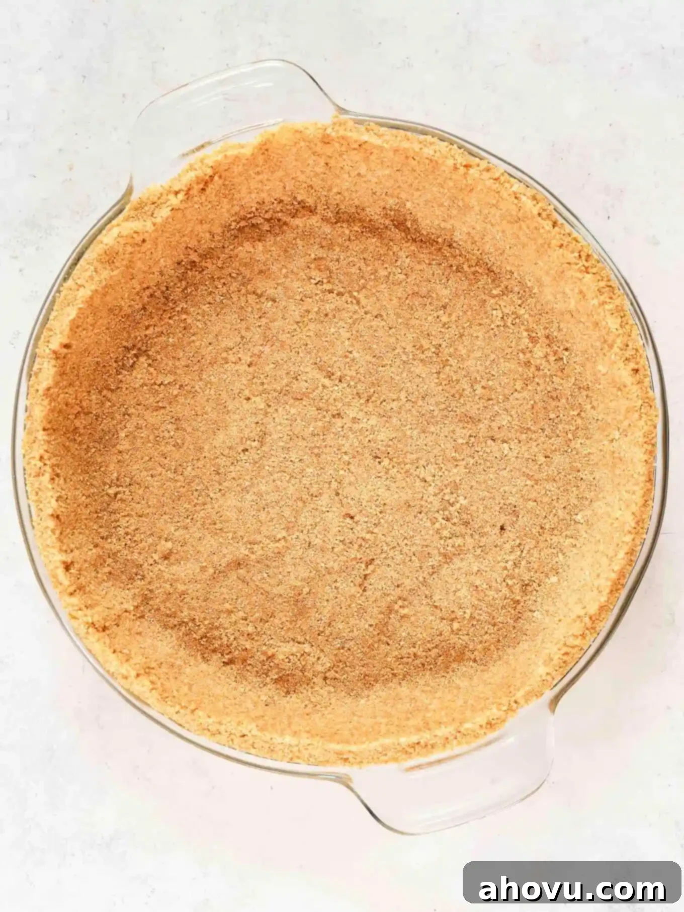 An overhead view of a perfectly pressed graham cracker crust in a pie dish, ready for the filling.