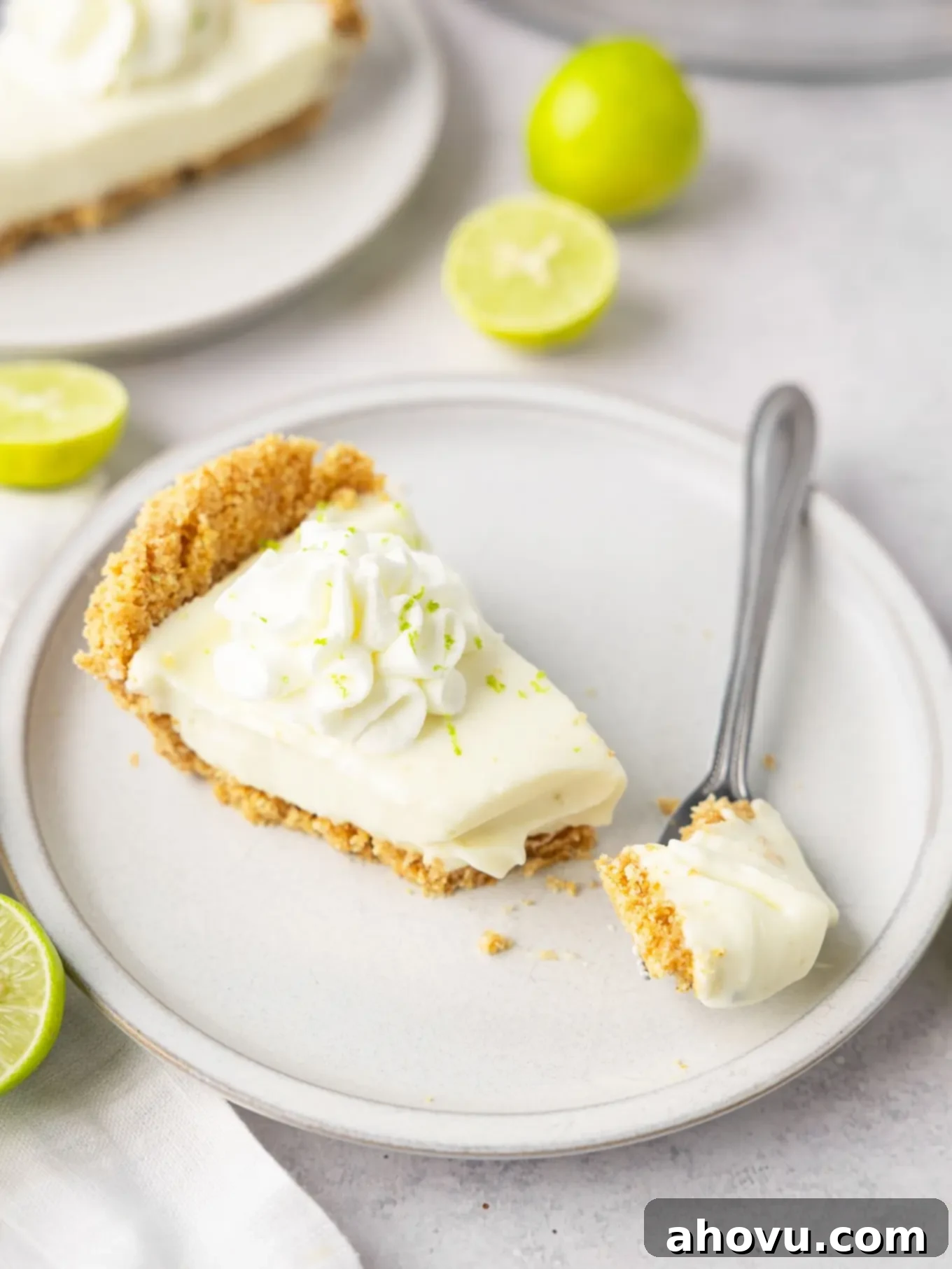 A delectable slice of no-bake key lime pie on a white plate, accompanied by a fork, showcasing its perfect texture and a hint of lime zest.