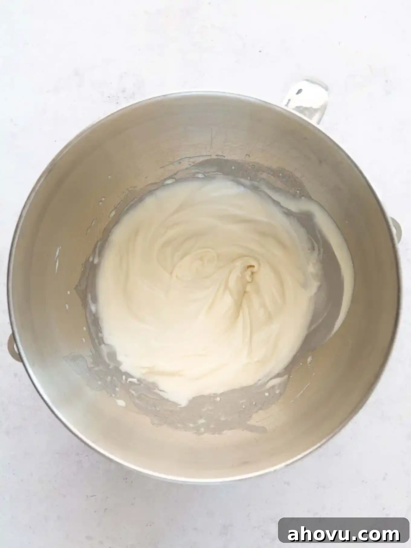 An overhead view of whipped cream with soft peaks in the bowl of a stand mixer. 