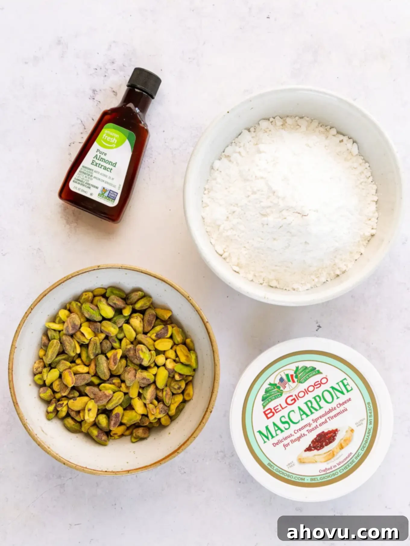 A countertop display of key ingredients: almond extract, cake flour, shelled pistachios, and mascarpone cheese, ready for baking.