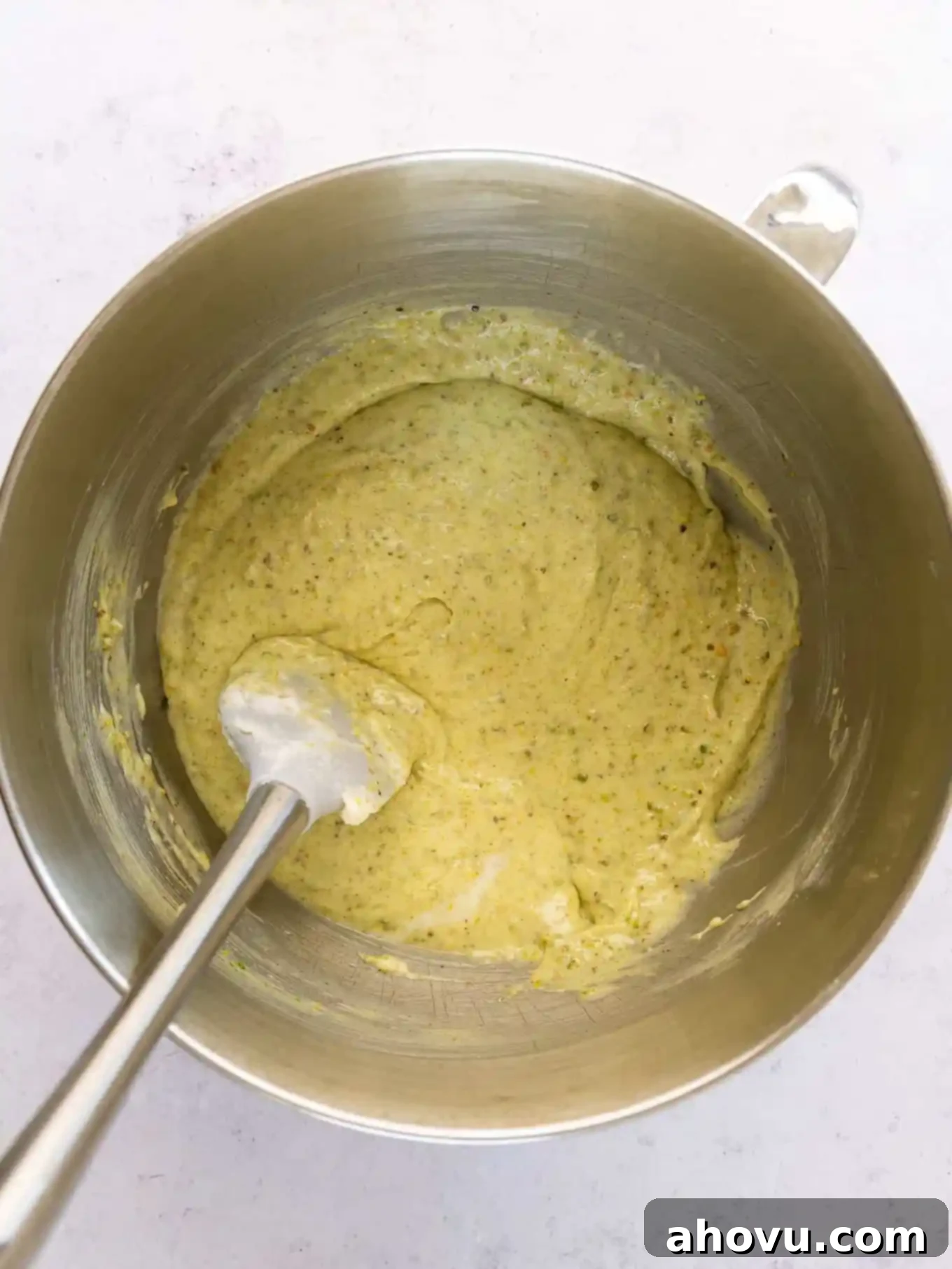 Pistachio cupcake batter in a mixing bowl, being gently folded with a rubber spatula.
