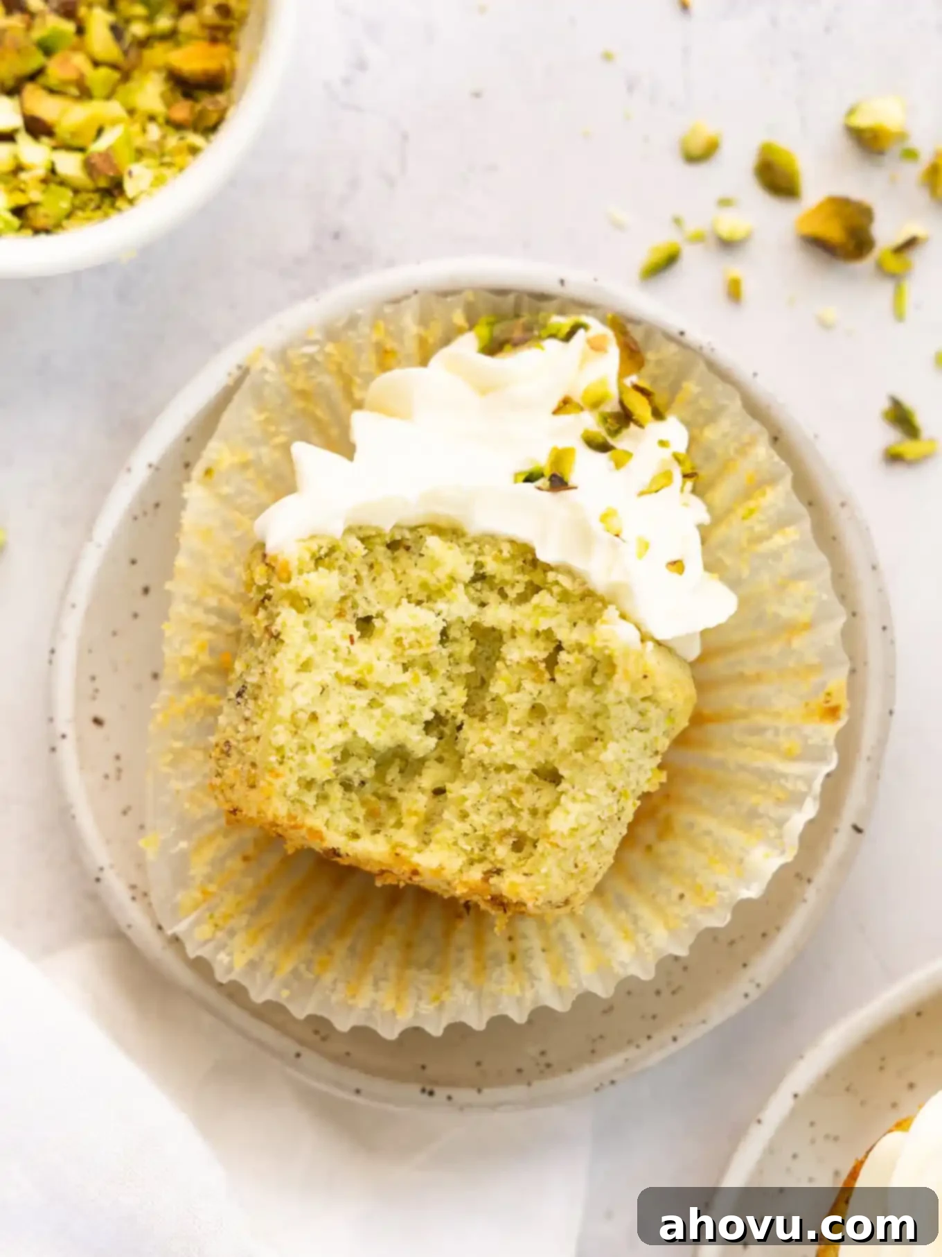 A pistachio cupcake with a bite taken out, turned on its side to reveal the moist, tender crumb and the delicious mascarpone frosting.