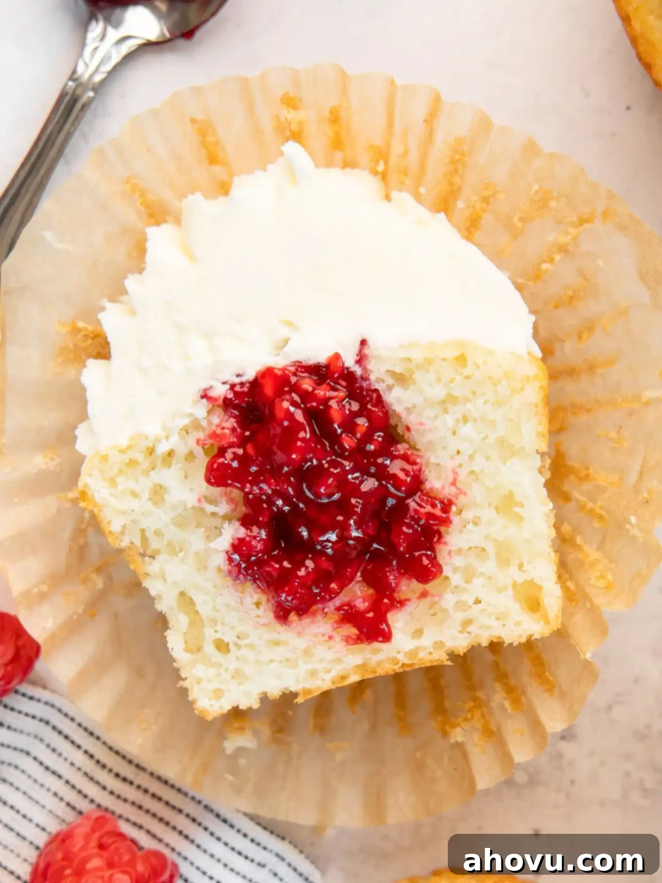 A white cupcake sliced in half, revealing a generous pocket of homemade raspberry filling nestled within its soft crumb.