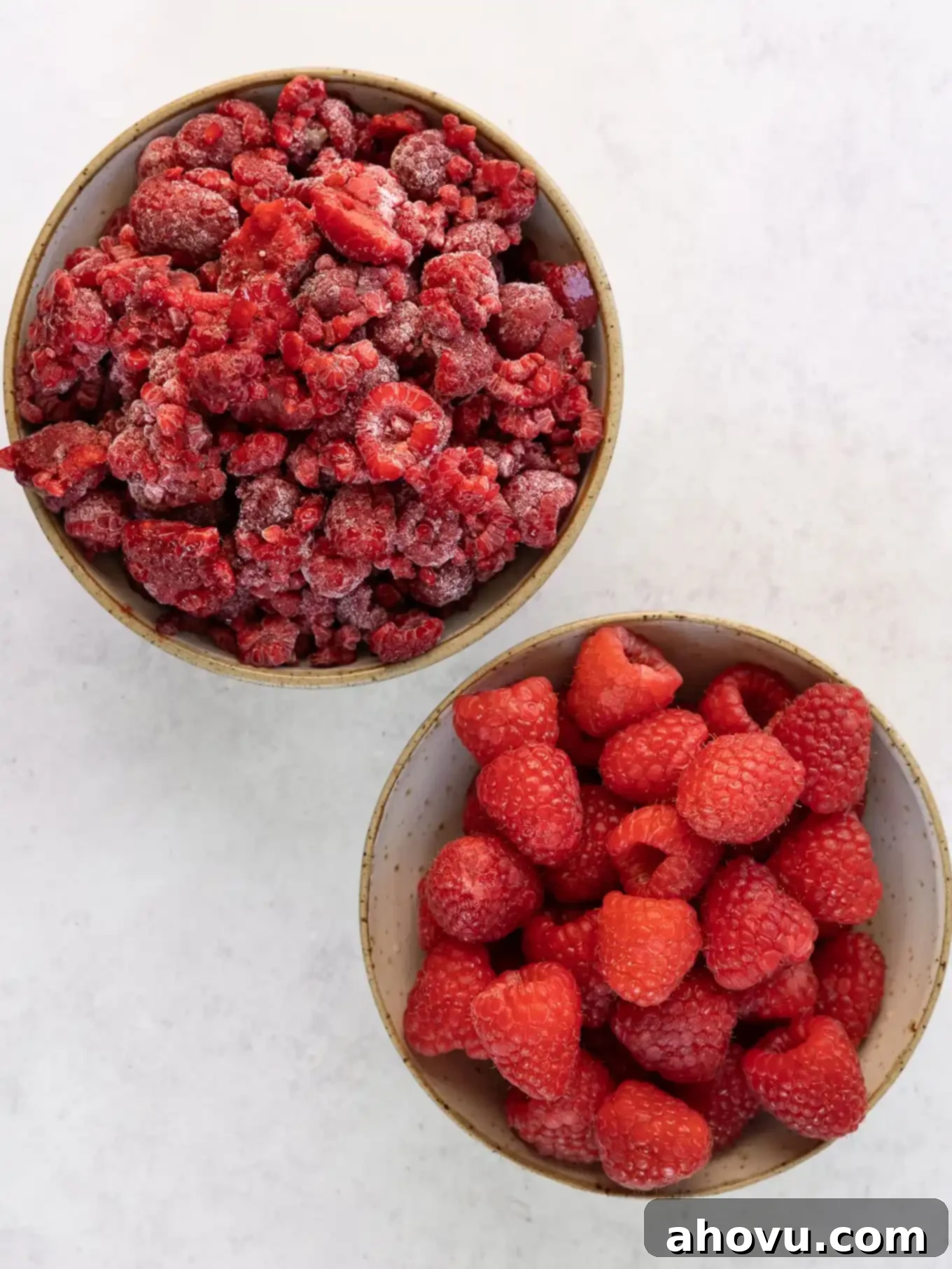 Two separate bowls showcasing the difference between fresh, plump raspberries and frozen, frosty raspberries, both perfect for this recipe.