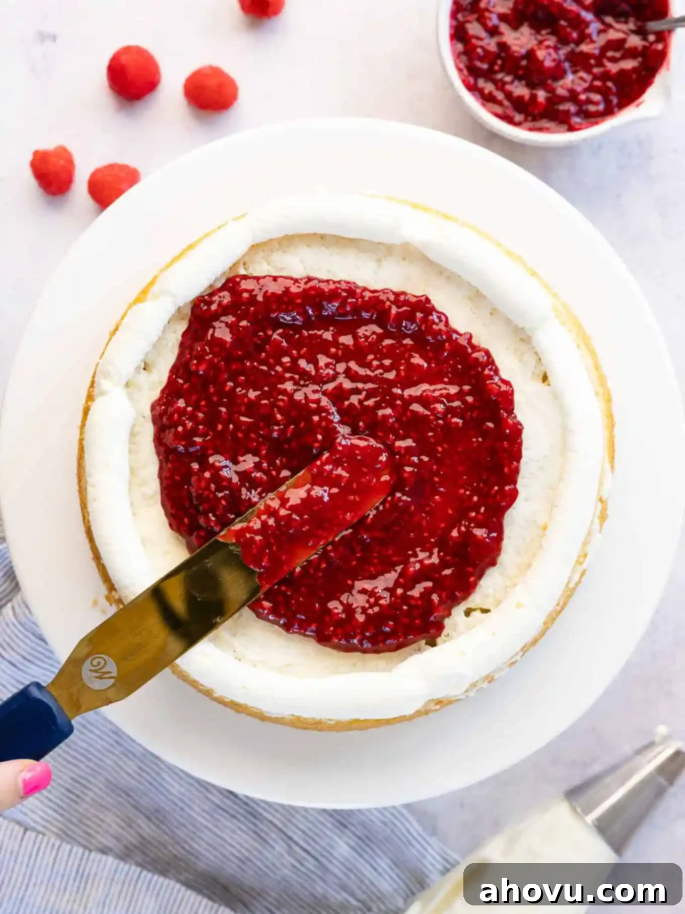 A layer cake being meticulously filled with the vibrant raspberry filling, demonstrating the technique for even distribution.