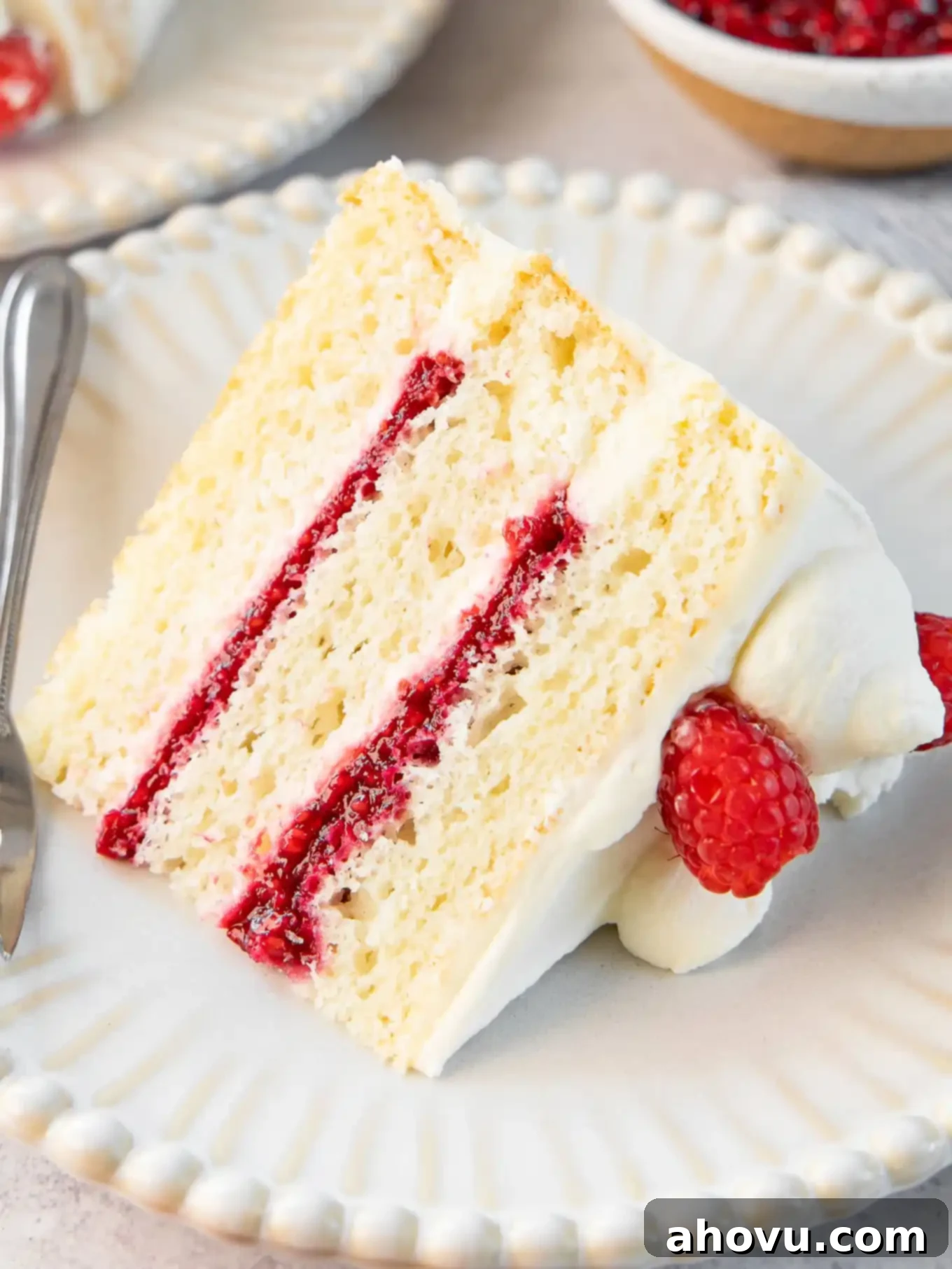 A tantalizing slice of white cake with beautiful, distinct layers of fluffy cake and vibrant raspberry cake filling.