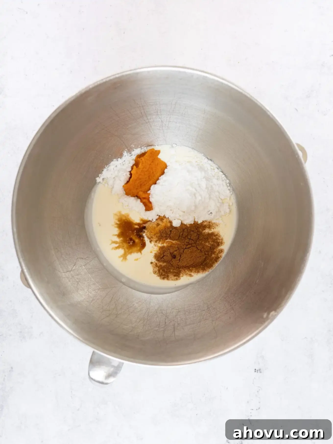 Heavy whipping cream, pumpkin puree, pumpkin pie spice, and vanilla extract combined in a chilled mixing bowl, ready for whipping.