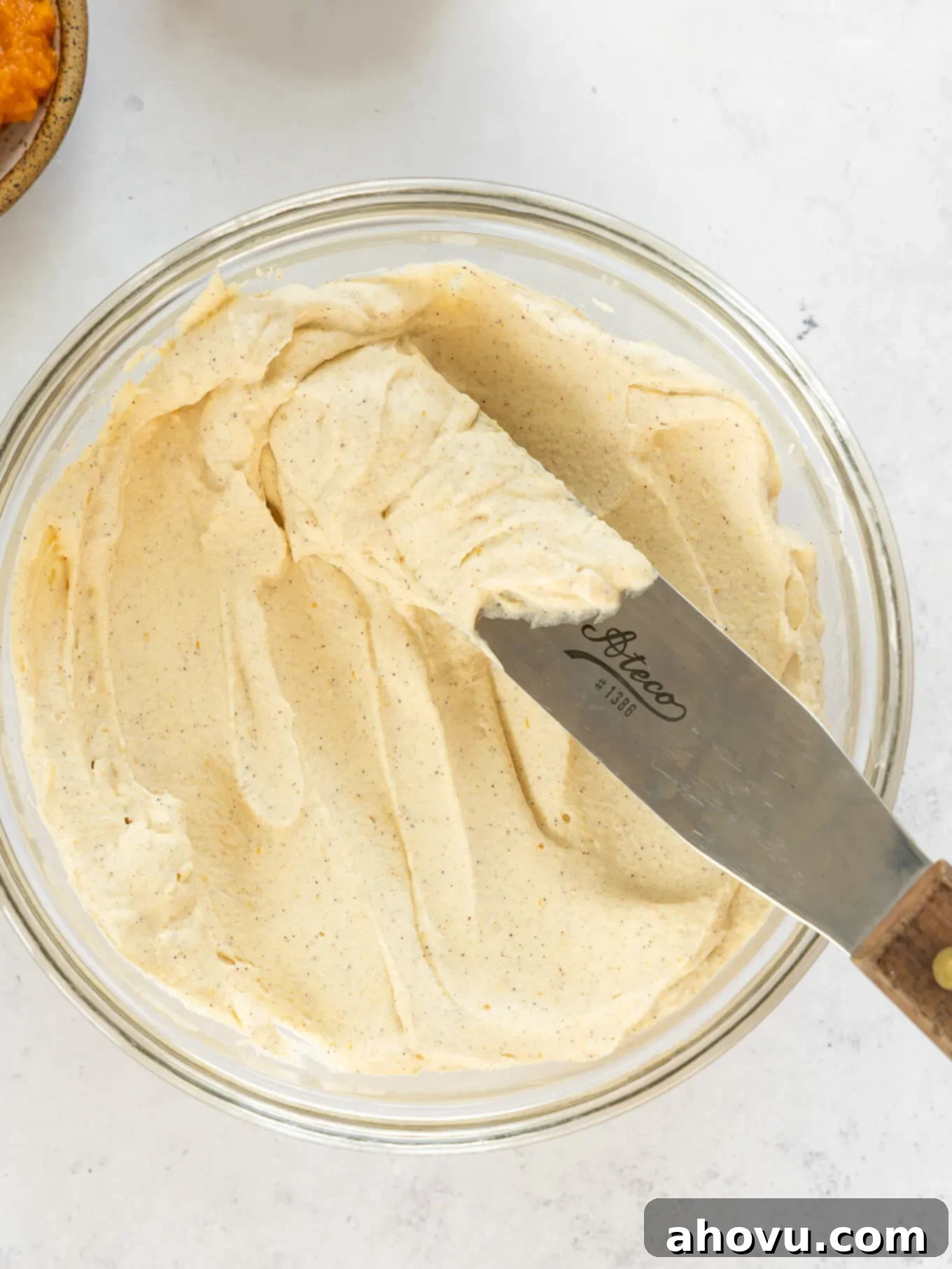 A bowl of pumpkin spice whipped cream, perfectly smooth and ready to be used, with an offset spatula resting beside it.