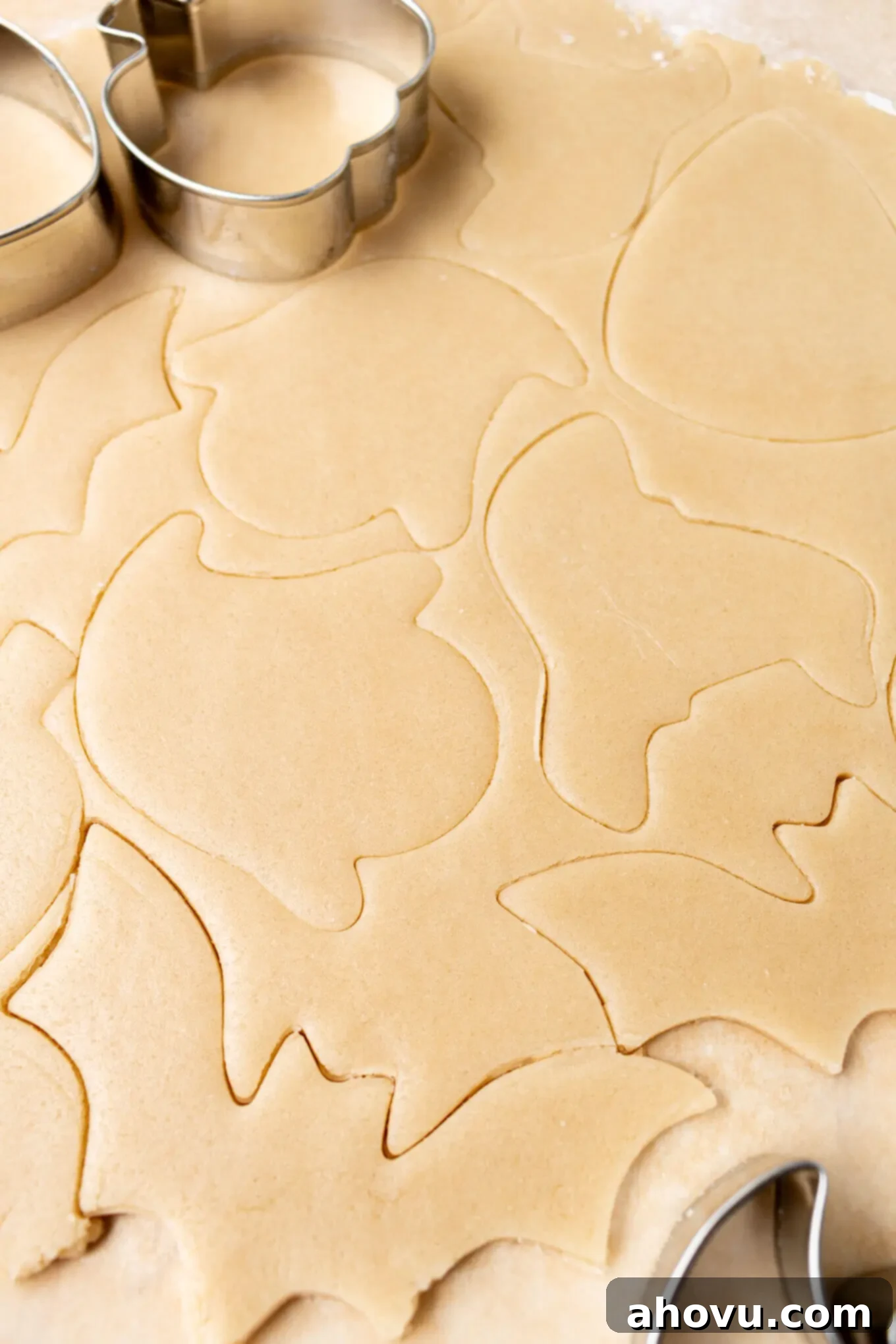 Frightfully Delicious Halloween Treats 4 Sugar cookie dough rolled out evenly between two sheets of parchment paper and cut into various Halloween shapes, ready for baking.
