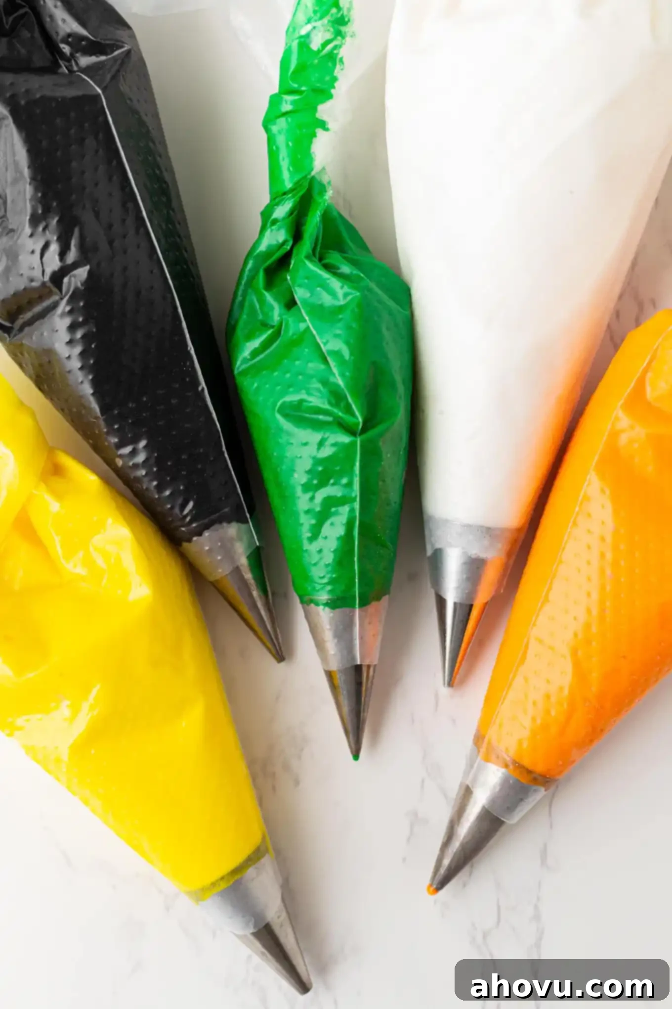 Frightfully Delicious Halloween Treats 7 Five piping bags, each filled with a different color of royal icing and fitted with a small round piping tip, ready for decorating.