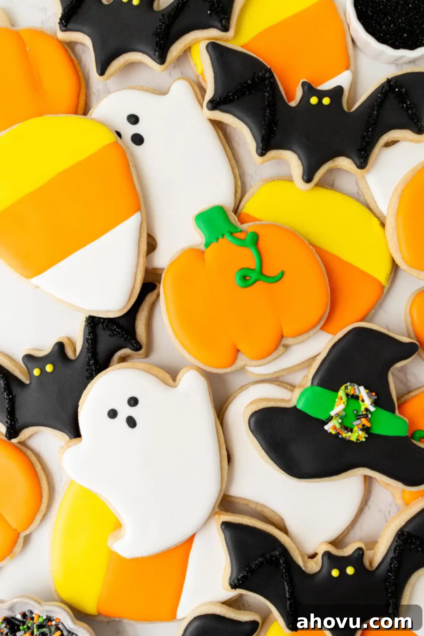 Frightfully Delicious Halloween Treats 10 An overhead view of a collection of meticulously decorated Halloween sugar cookies featuring various designs like bats, ghosts, pumpkins, and witches' hats, all topped with shiny royal icing.