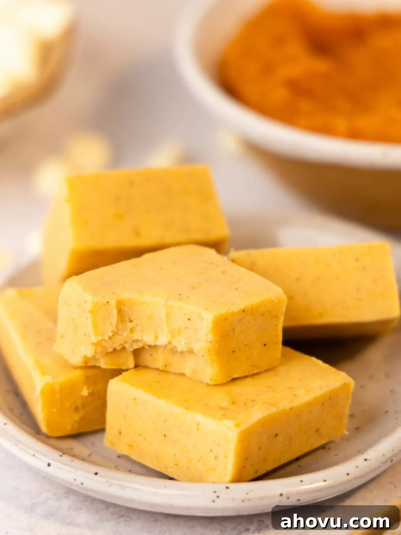 Pumpkin Spice Fudge 9 Multiple slices of vibrant orange pumpkin fudge displayed on a plate, with one piece showing a bite taken out, inviting tasting.