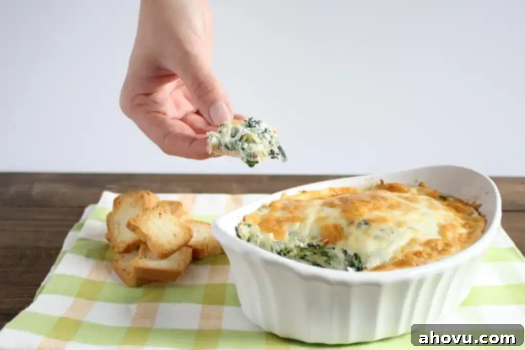 No mayo spinach artichoke dip being scooped out of a white baking dish that rests on a tea towel. 