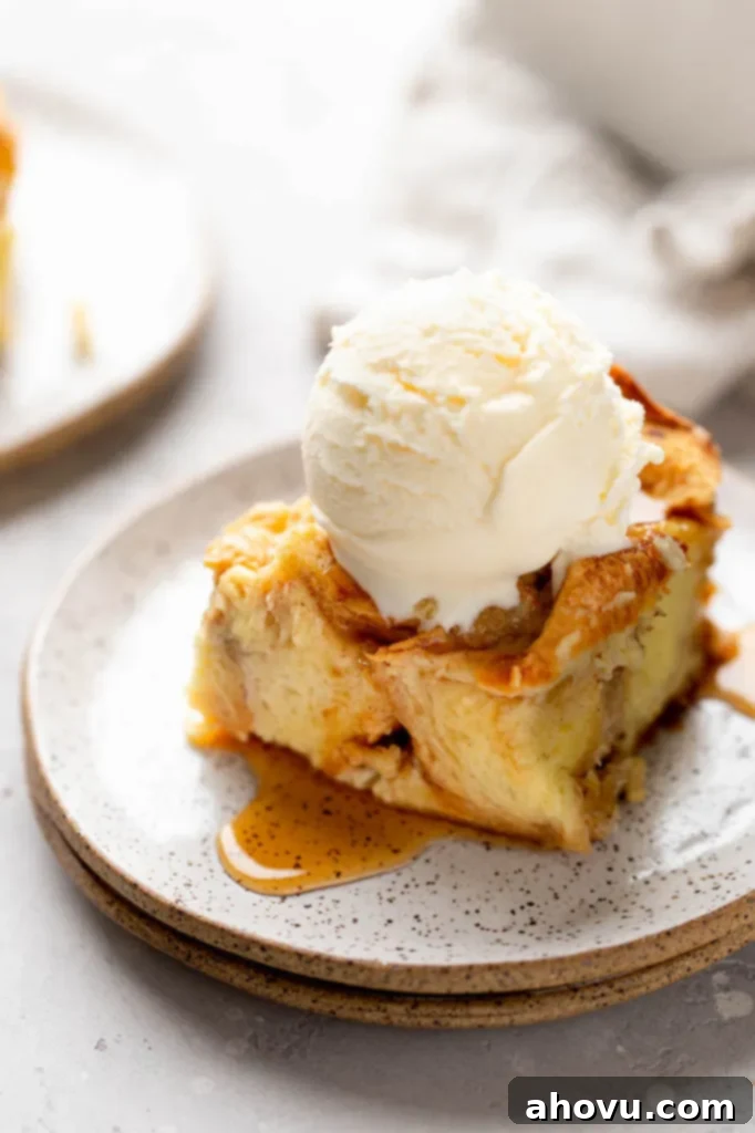 A slice of bread pudding topped with a scoop of ice cream on a white speckled plate, highlighting its creamy texture.