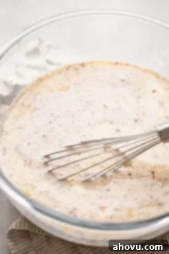 A glass bowl with a whisk, showcasing the creamy egg custard mixture for bread pudding.