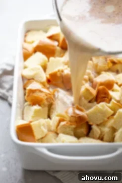 The rich egg custard mixture being carefully poured over the cubed bread in a 9x13 baking pan, ensuring even saturation.