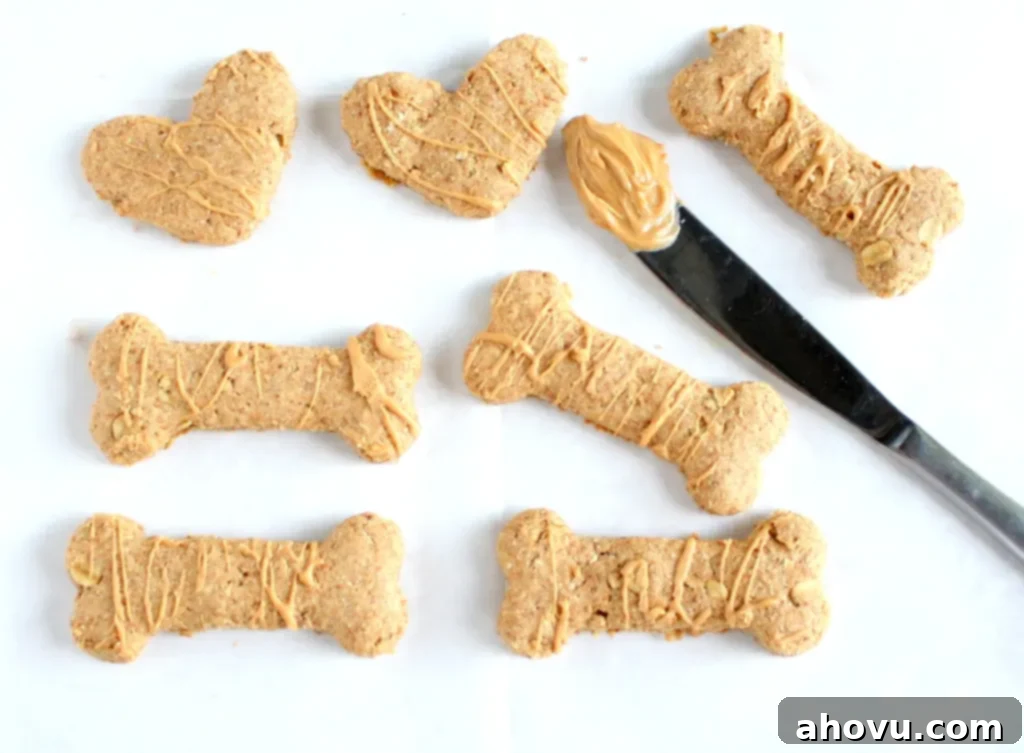 Overhead view of homemade peanut butter dog treats in various shapes. A knife with peanut butter on it rests in the middle. 