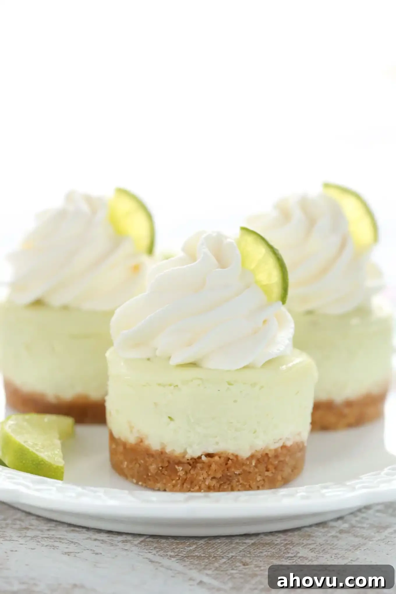 A side view of three key lime mini cheesecake bites on a white plate, showcasing their perfect individual size.