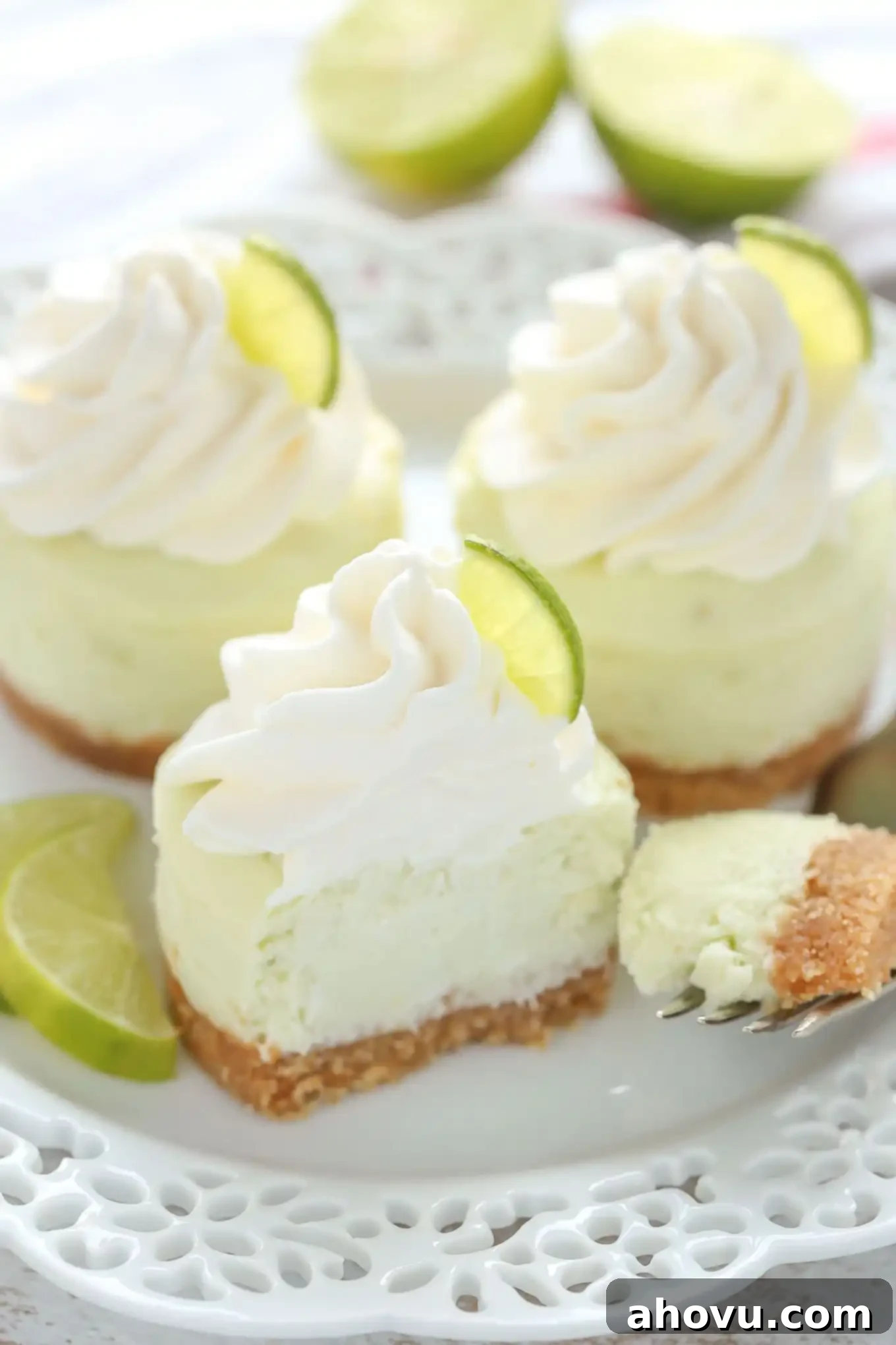 A white plate with three mini key lime cheesecakes, garnished with a lime wedge and a fork, ready to be enjoyed.
