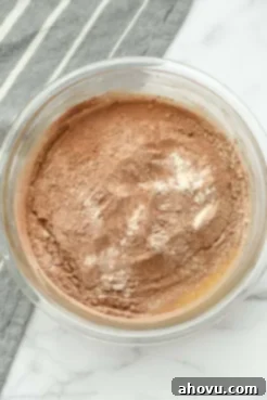 A clear mixing bowl showing wet ingredients topped with sifted dry ingredients for homemade fudgy brownies.