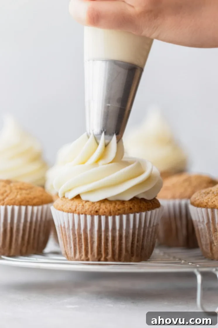 Velvet Cream Cloud 5 A group of cupcakes on a round cooling rack being topped with cream cheese frosting.