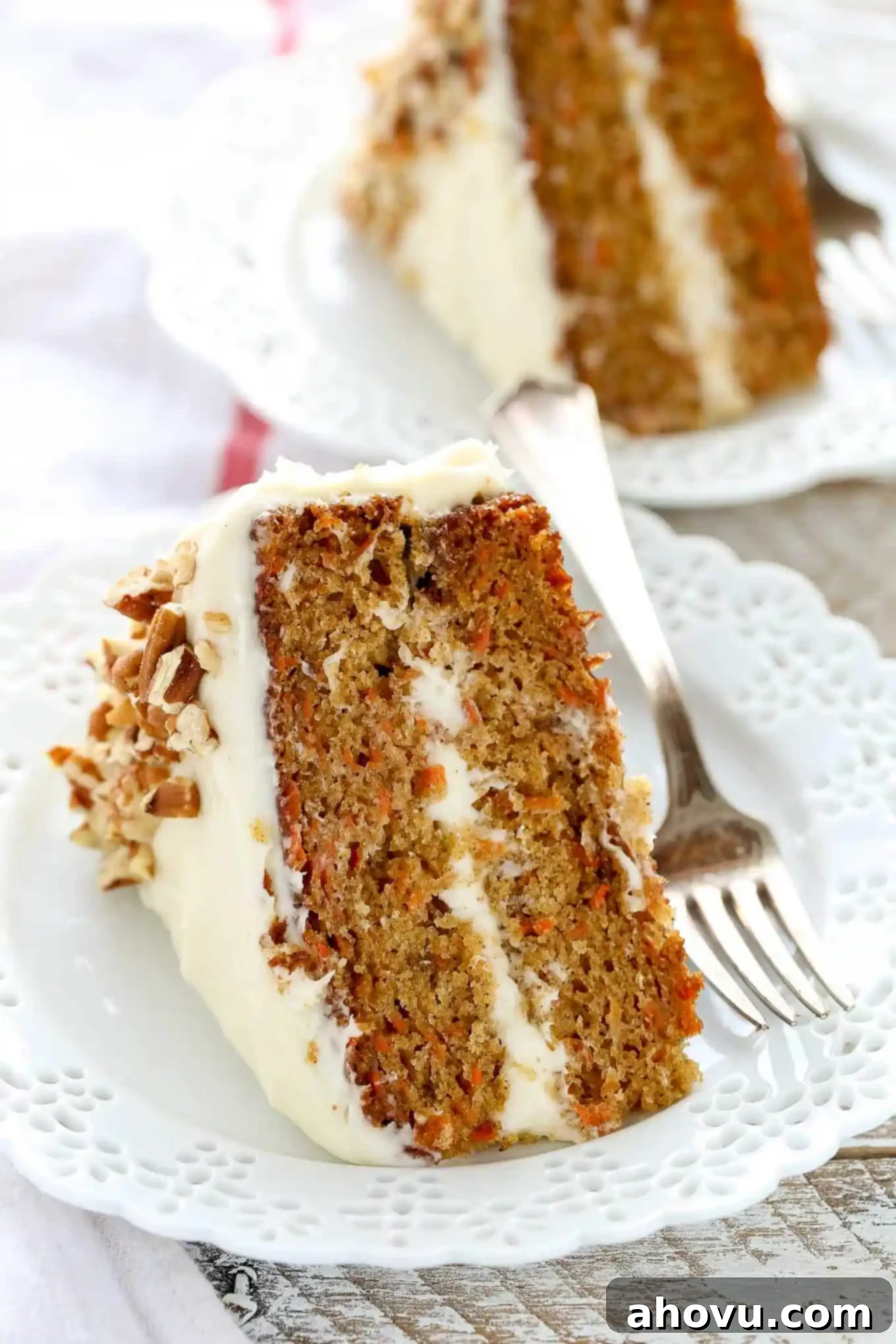Irresistible Carrot Cake Delight 2 Two generous slices of beautifully frosted carrot cake, each resting on separate decorative white plates with a fork positioned elegantly beside them.