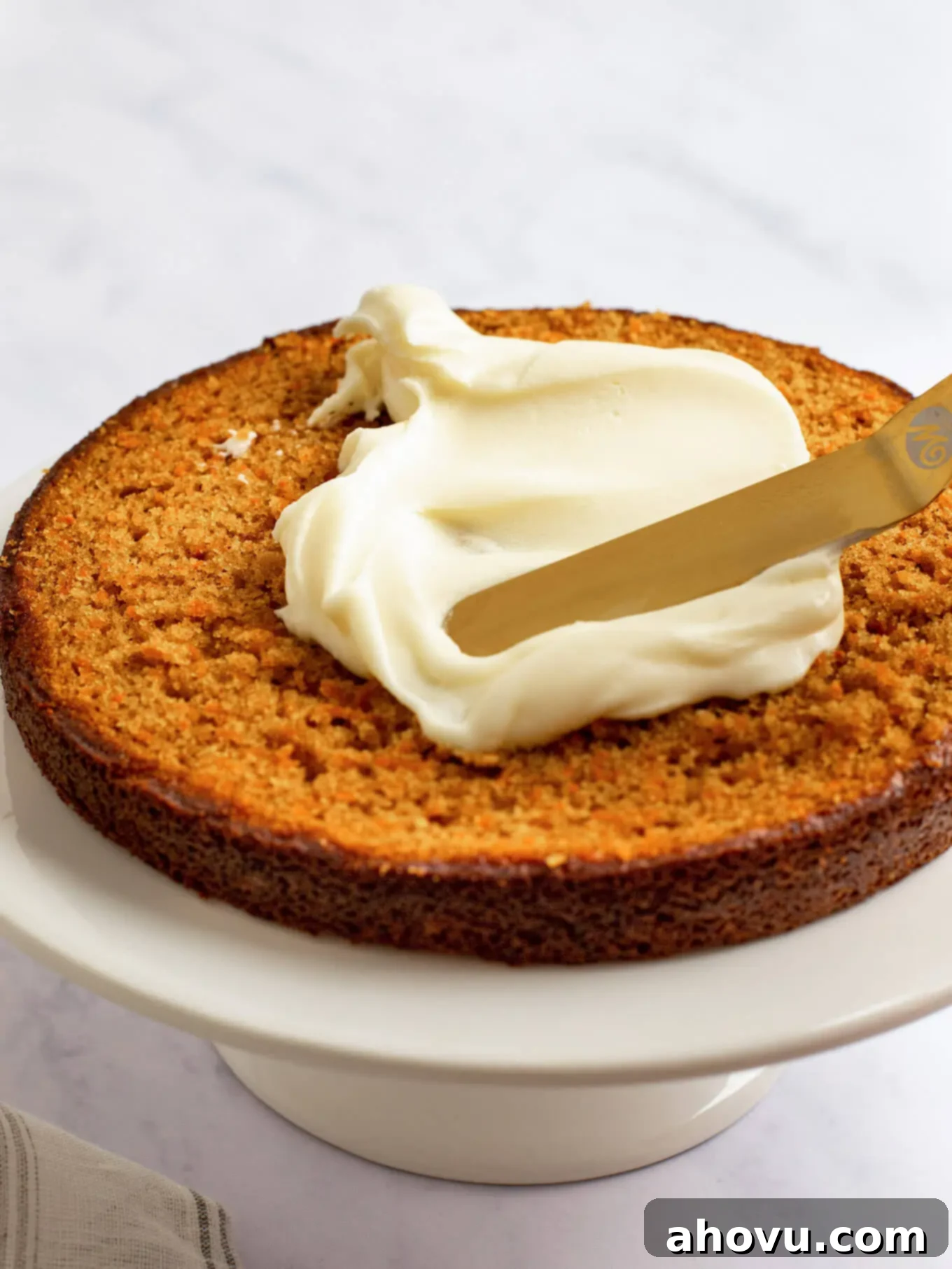 Irresistible Carrot Cake Delight 11 A slice of carrot cake resting on a cake stand, with luscious cream cheese frosting being expertly spread across its surface using a spatula.