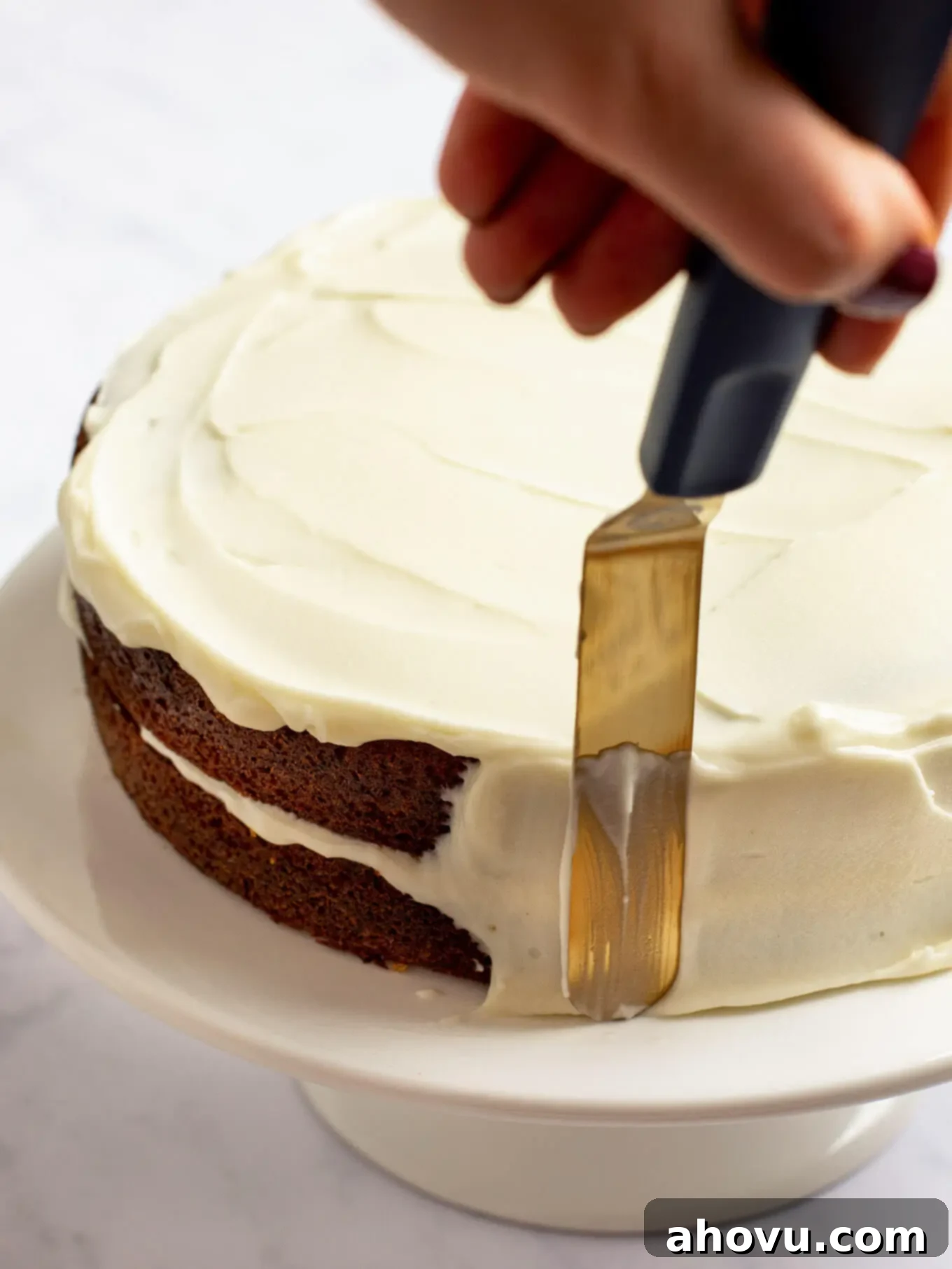 Irresistible Carrot Cake Delight 12 A beautifully assembled two-layer carrot cake being frosted on both the top and sides with smooth, white cream cheese frosting, ready for its final touches.