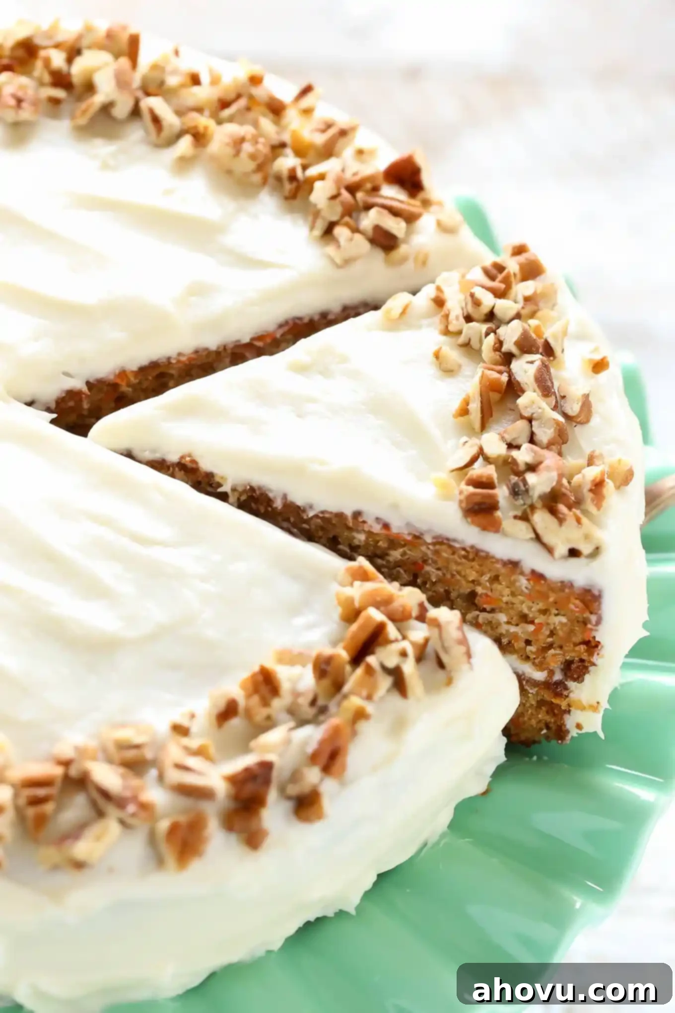 Irresistible Carrot Cake Delight 13 A fully assembled and frosted carrot cake proudly displayed on a vibrant green cake stand, generously topped with creamy frosting and a scattering of chopped pecans for garnish.