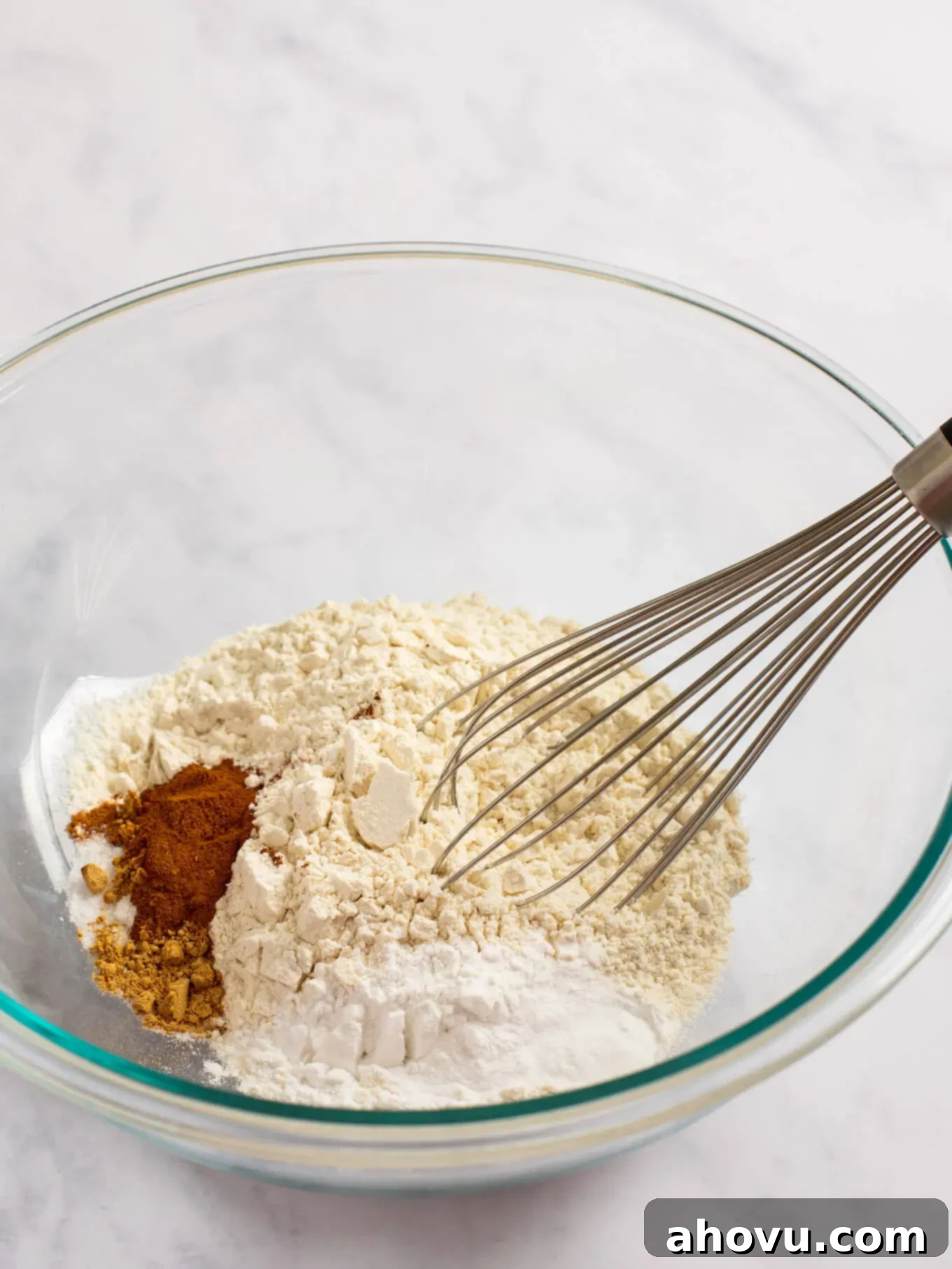 Irresistible Carrot Cake Delight 4 A large glass mixing bowl filled with the dry ingredients for carrot cake: flour, various spices, baking powder, baking soda, and salt, perfectly combined.