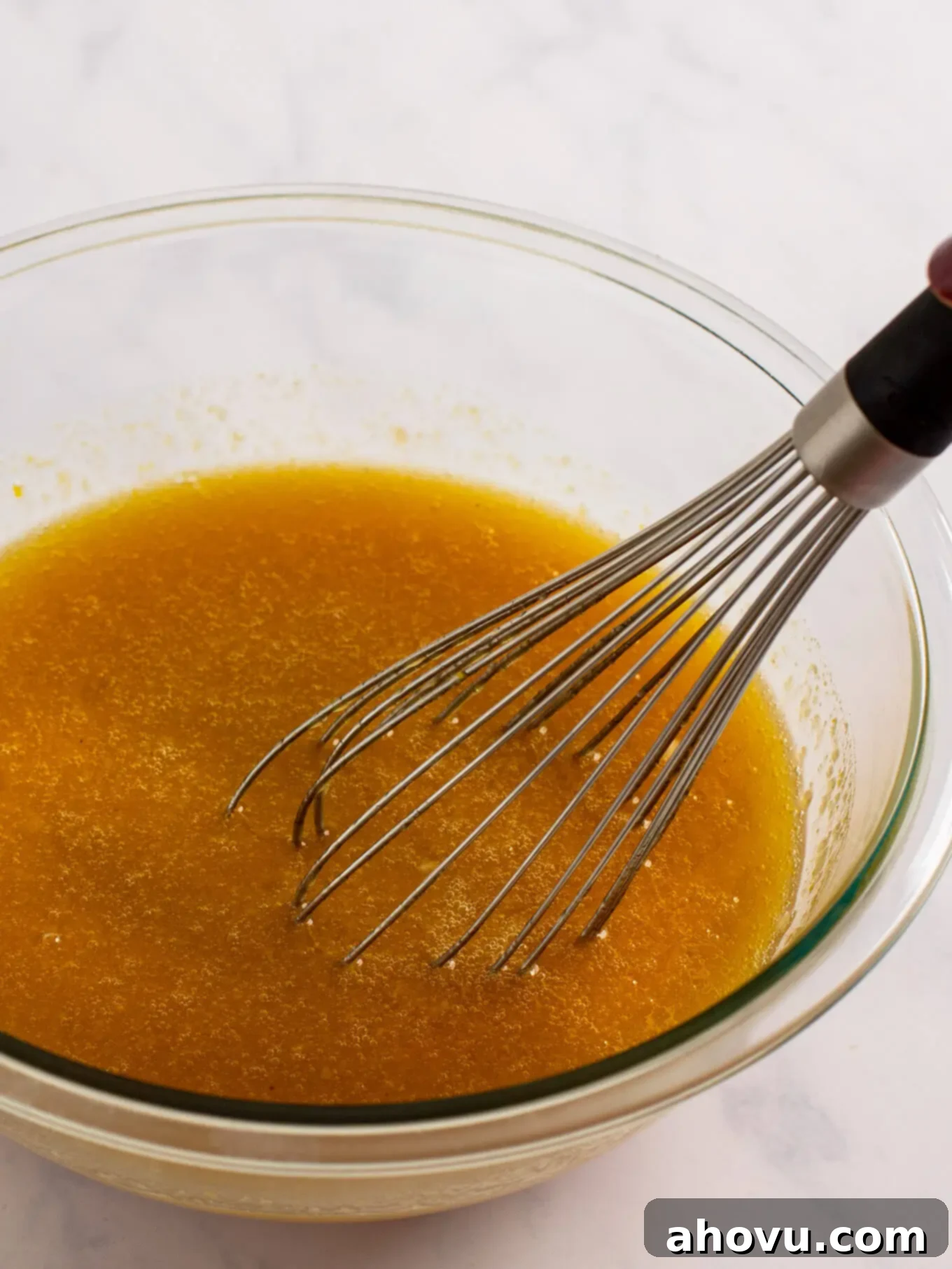 Irresistible Carrot Cake Delight 5 The wet ingredients for the carrot cake, including oil, eggs, sugars, applesauce, and vanilla extract, thoroughly whisked together in a separate glass mixing bowl, creating a smooth mixture.