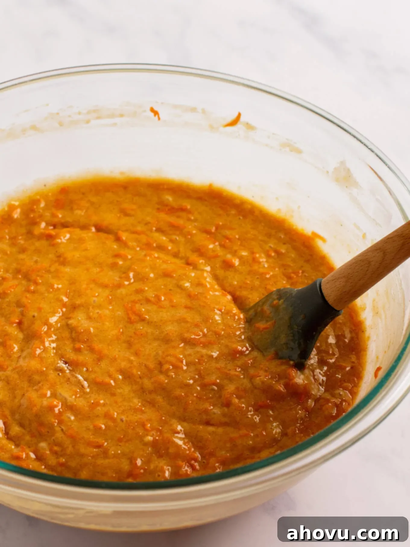 Irresistible Carrot Cake Delight 7 The finished carrot cake batter, rich with grated carrots, in a large glass mixing bowl, ready for baking. A rubber spatula is poised on the edge of the bowl.