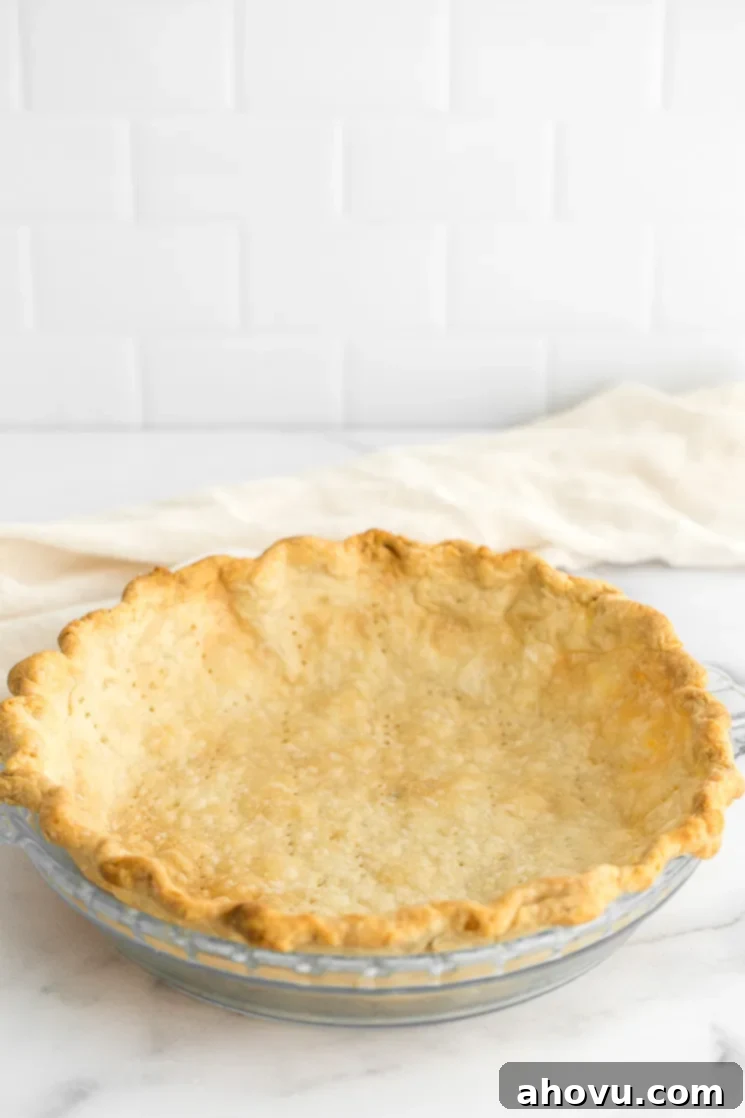 A pristine, homemade pie crust, perfectly golden and fluted, resting in a ceramic pie dish on a sleek marble surface, ready for filling.