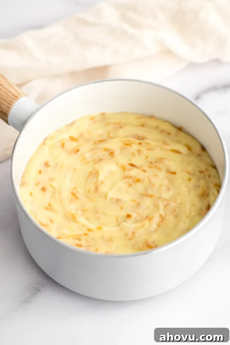 A close-up view of the rich, golden-yellow coconut cream pie filling simmering gently in a white saucepan on a stovetop, indicating its creamy texture.