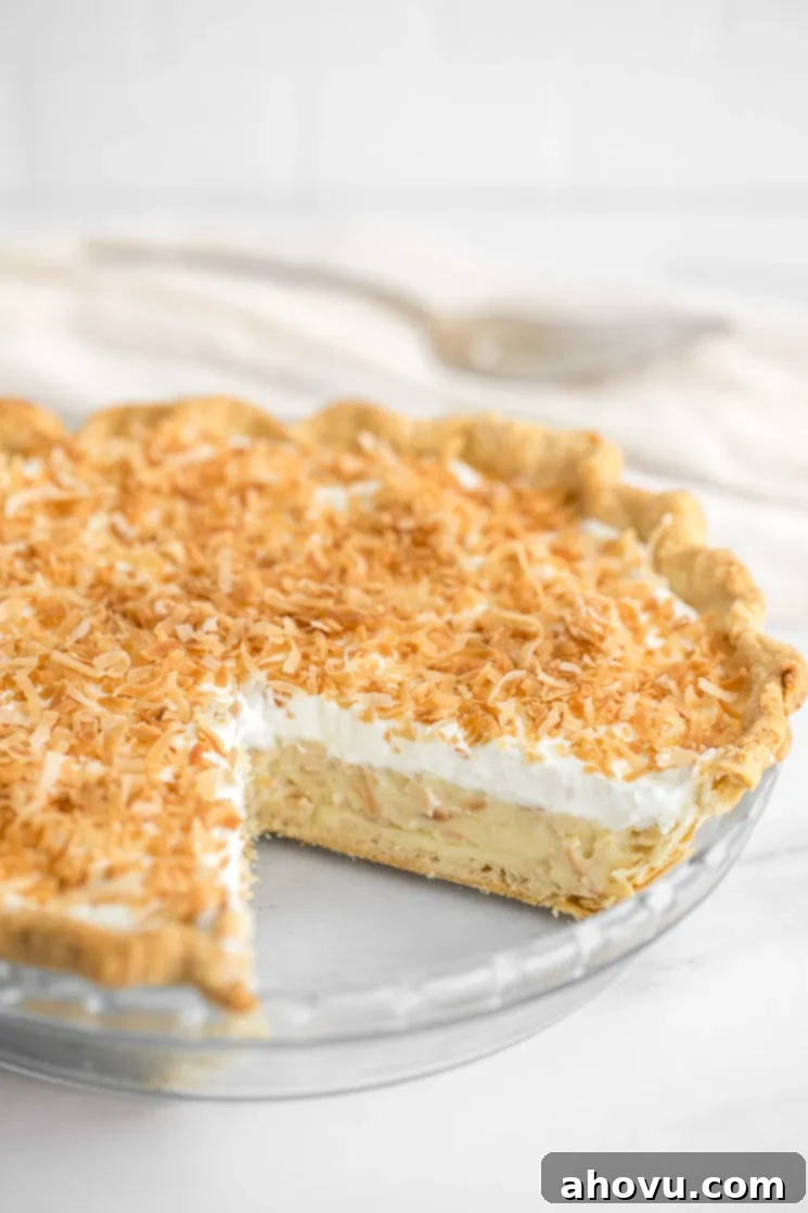 A tempting close-up of a full coconut cream pie with a perfect slice already removed, revealing the creamy layers and inviting texture.