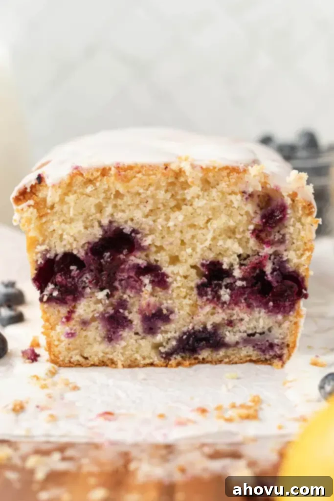 A front view of a loaf of lemon blueberry bread, sliced to show the interior with blueberries and a thick lemon glaze on top.