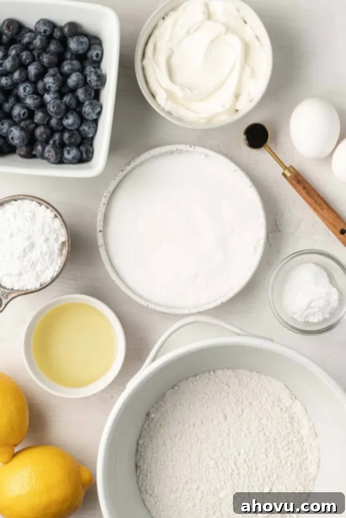 An overhead view of the fresh ingredients neatly arranged on a white surface, including lemons, blueberries, flour, sugar, oil, sour cream, and eggs, ready to make blueberry lemon bread with lemon glaze.