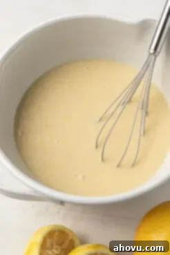 Lemon quick bread batter in a large mixing bowl, with a whisk resting inside, showing a smooth, creamy texture.