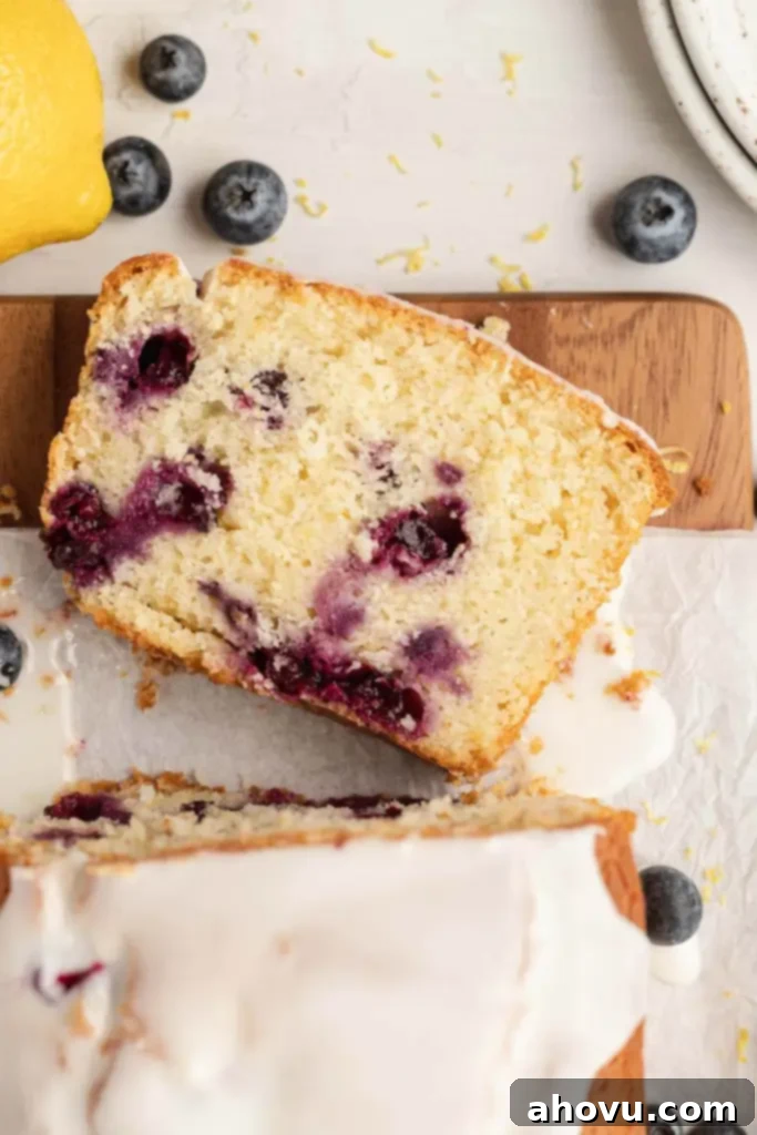 An overhead view of a lemon blueberry bread on a wood cutting board, with one slice elegantly lying on its side, showcasing the moist interior.